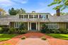 Stone and clapboard exterior featuring a covered entryway with columns, a shingled roof with a chimney, and a multi-patterned brick walkway