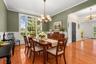 An elegant formal dining room showcases expansive windows, gleaming pinewood plank floors, decorative molding, and a glowing chandelier, creating a so