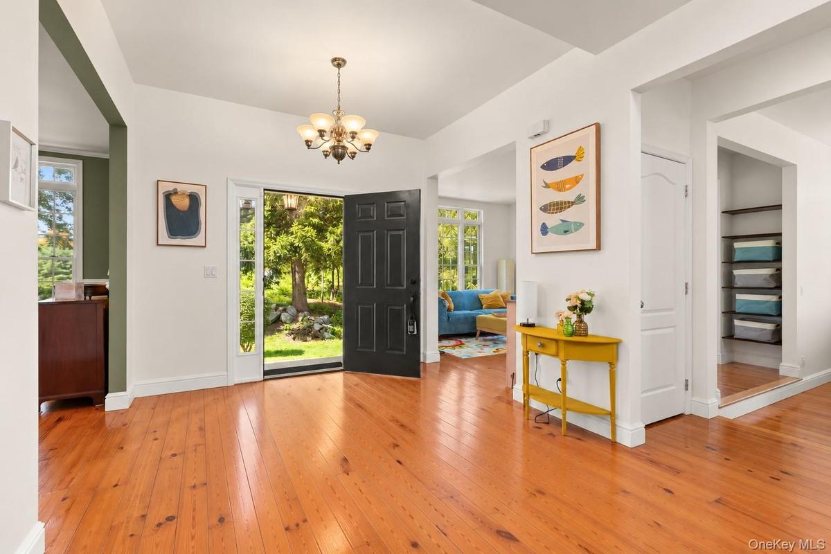 A welcoming, light-filled foyer features gleaming pinewood floors, high ceilings with architectural soffit detailing, and an open, airy design that se
