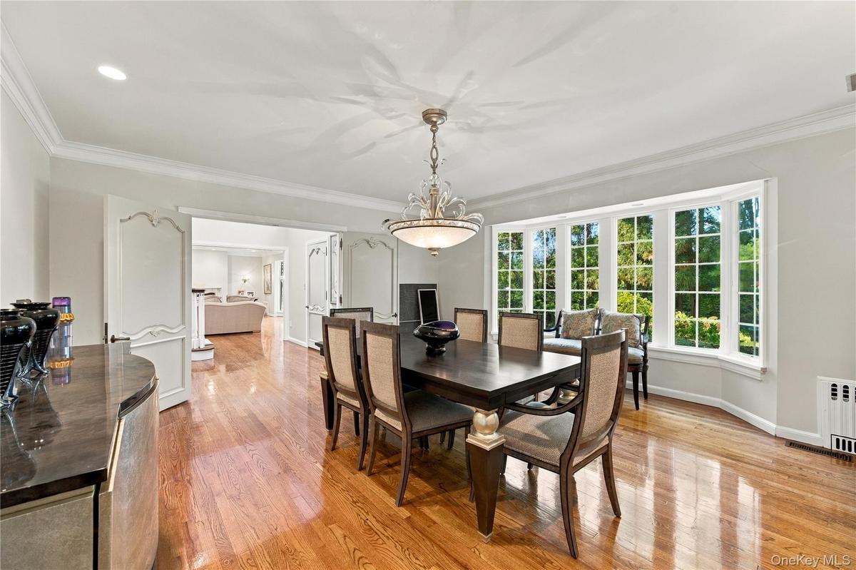 Dining area featuring wood-finish flooring, crown molding, an expansive bay window, and a decorative tiered chandelier
