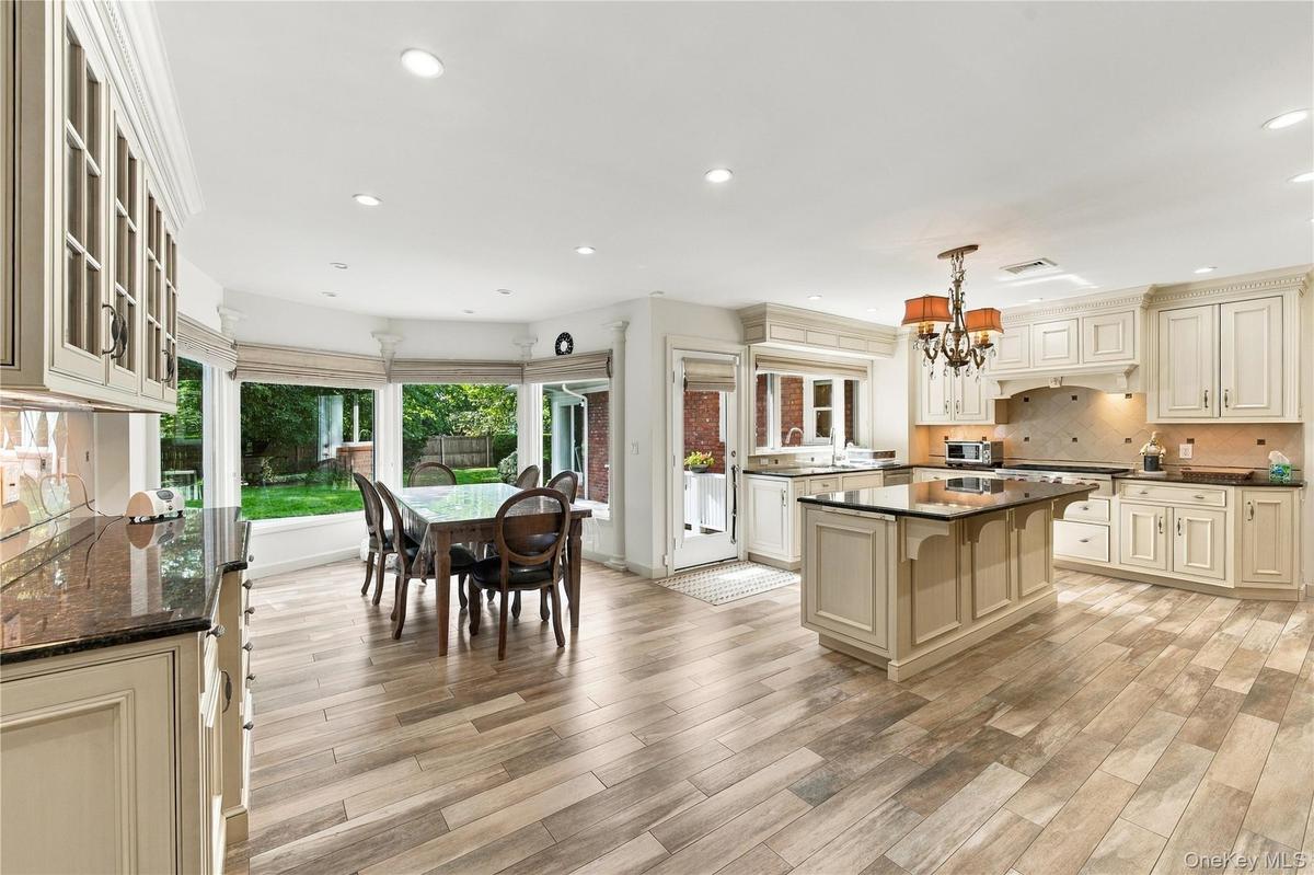Kitchen featuring wood-finish flooring, custom cabinetry, central island with stone countertop, tile backsplash, and bay windows