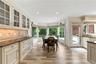 Kitchen featuring custom cabinetry with glass-front uppers, stone countertops, tiled backsplash, wood-finish flooring, and a bay window configuration