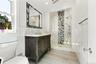 Dark wood-finish vanity with a stone countertop, glass-enclosed shower with mosaic tile inlay, decorative mosaic-framed mirror, and textured wall tile