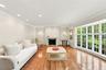 Living area featuring hardwood flooring, a decorative stone-surround fireplace, crown molding, recessed lighting, and expansive multi-pane windows