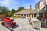 Spacious stone patio featuring a curved brick retaining wall, multi-tonal slate roof tiles, brick exterior siding, and a striped retractable awning