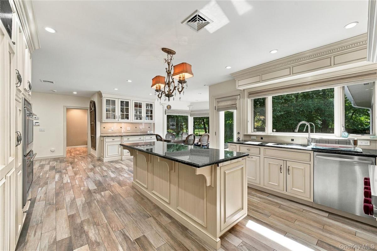 Kitchen featuring custom cabinetry with crown molding, a center island with a dark stone countertop, stainless steel appliances, wood-finish flooring,