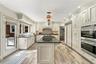 Kitchen featuring light-toned recessed-panel cabinetry, a central island with stone-finish countertops, stainless steel double wall ovens, wood-finish