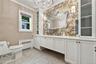 Custom white cabinetry with integrated storage, antique-style mirrored backsplash, metallic light fixtures, and stone-tiled flooring