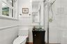 Bathroom featuring white wall tiling with chair rail molding, a dark wood-finish vanity with a glass vessel sink, a chrome faucet, and a glass-enclose