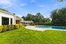 Expansive rear grounds featuring a curved stone pool deck, in-ground swimming pool, manicured lawn, and mature perimeter trees