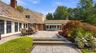 Expansive stone patio featuring a multi-level terrace, brick retaining wall, retractable fabric awning, and slate-style shingle roof