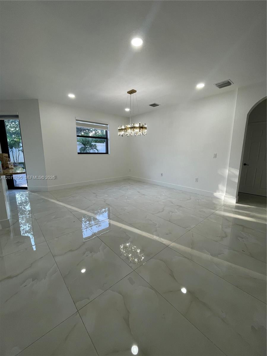 Large-format tile flooring, recessed ceiling lighting, crystal chandelier, and arched doorway entry