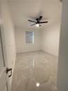 Large-format neutral tile flooring, matte black ceiling fan with integrated lighting, and window with installed dual-shade roller blinds