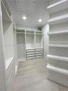 Custom walk-in storage featuring floor-to-ceiling white shelving, integrated drawer banks, hanging rods, and light-toned wood-finish flooring
