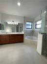 Bathroom featuring a double-sink vanity with wood cabinetry, a large wall-mounted mirror, a separate glass-enclosed shower, and a built-in soaking tub