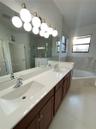 Dual-sink vanity with a solid-surface countertop, dark wood-finish cabinetry, large wall-mounted mirror, multi-globe light fixture, and corner soaking