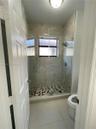 Walk-in shower featuring floor-to-ceiling tile, a frameless glass enclosure, pebble-stone shower floor, and a wall-mounted shower head, complemented b