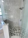 Walk-in shower with floor-to-ceiling large-format tile surround, hexagonal patterned floor tile, glass enclosure, and a square rainfall showerhead