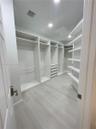 Walk-in closet featuring floor-to-ceiling white custom built-in cabinetry, integrated drawer storage, open shelving, and wood-finish flooring