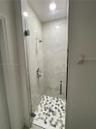 Walk-in shower featuring large-format stone-finish wall tile, a frameless glass door, a metallic hand-held shower head, and decorative hexagonal floor