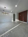 Large-format polished tile flooring, vertical wood-slat accent wall, recessed lighting, crystal-style chandelier, and arched doorway