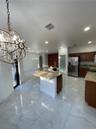 Kitchen featuring stone-finish countertops, dark wood cabinetry, large-format tile flooring, a center island with an integrated sink, and an ornamenta