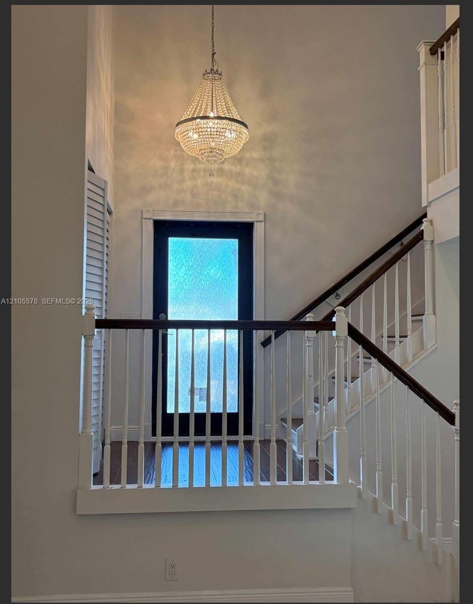 Grand entryway featuring a high-reaching ceiling, crystal-accented chandelier, staircase with wood-finish handrail, and a glass-paneled door