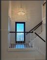 Grand entryway featuring a high-reaching ceiling, crystal-accented chandelier, staircase with wood-finish handrail, and a glass-paneled door