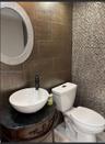 Oval vessel sink with a dark-finish faucet, stone-top vanity, textured wall tiling, and decorative mosaic accent wall