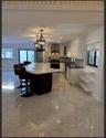 Kitchen featuring a large central island with light-toned stone-finish countertop, white cabinetry, dark stone-finish perimeter counters, polished til