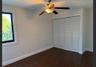 Interior room featuring wood-finish flooring, a multi-pane window with white trim, a ceiling fan with integrated lighting, and a bi-fold louvered clos