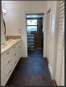 Bathroom featuring a white cabinetry vanity, stone-patterned countertop with a mosaic tile backsplash, slate-finish floor tile, and a textured stone w