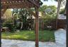 Backyard featuring a wooden pergola, stone-tile patio, wood privacy fencing, a stone water feature, and mature tropical landscaping