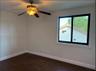 Room featuring dark wood-finish flooring, a ceiling fan with integrated lighting, and a window framed by white molding