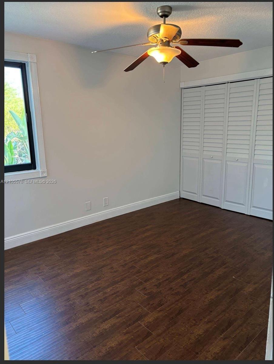 Wood-finish flooring, white louvered-panel closet doors, and ceiling-mounted light fixture with a fan