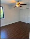 Wood-finish flooring, white louvered-panel closet doors, and ceiling-mounted light fixture with a fan