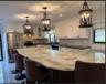 Kitchen featuring a large central island with light-toned natural stone surfacing, white cabinetry, dark countertops, tiled backsplash, and decorative