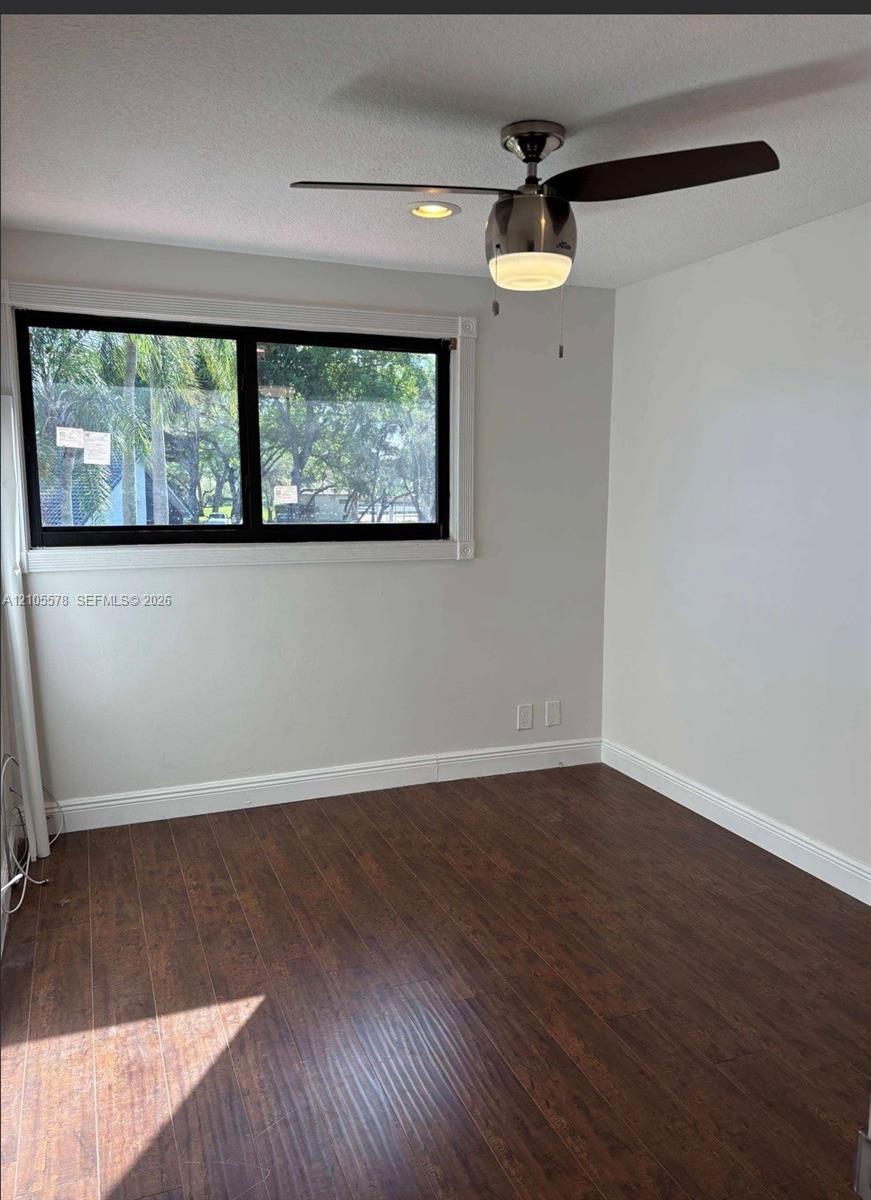 Room featuring dark wood-finish flooring, a large horizontal window with a black frame, and a brushed-metal ceiling fan with integrated lighting