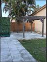 Rear exterior space featuring a wooden pergola, concrete paver patio, tall wooden privacy fencing, and established palm trees