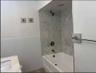 Bathtub with stone-finish tile surround, white subway tile wainscoting, integrated countertop vanity, and metal fixtures