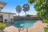 Freeform swimming pool with a metal grab rail, surrounded by a brick paver patio and enclosed by a wood privacy fence