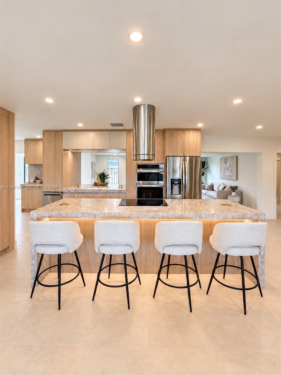 Kitchen featuring a central island with integrated cooktop, stone-finish countertops, stainless steel cylindrical range hood, custom wood-finish cabin