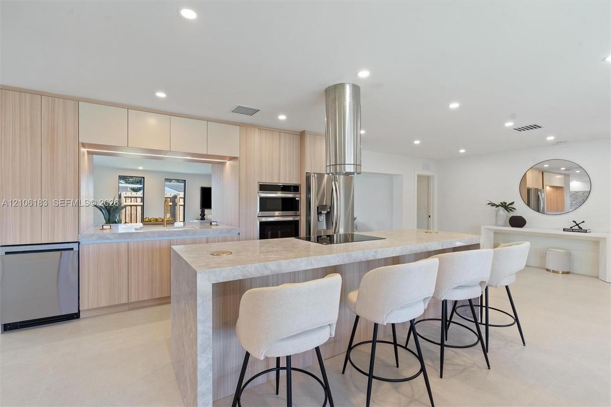 Contemporary kitchen featuring a large waterfall-edge island with light stone countertops, stainless steel appliances including a built-in double oven