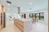 Kitchen featuring a central island with a waterfall-edge stone countertop, cylindrical stainless steel range hood, built-in wall oven, flat-panel cabi