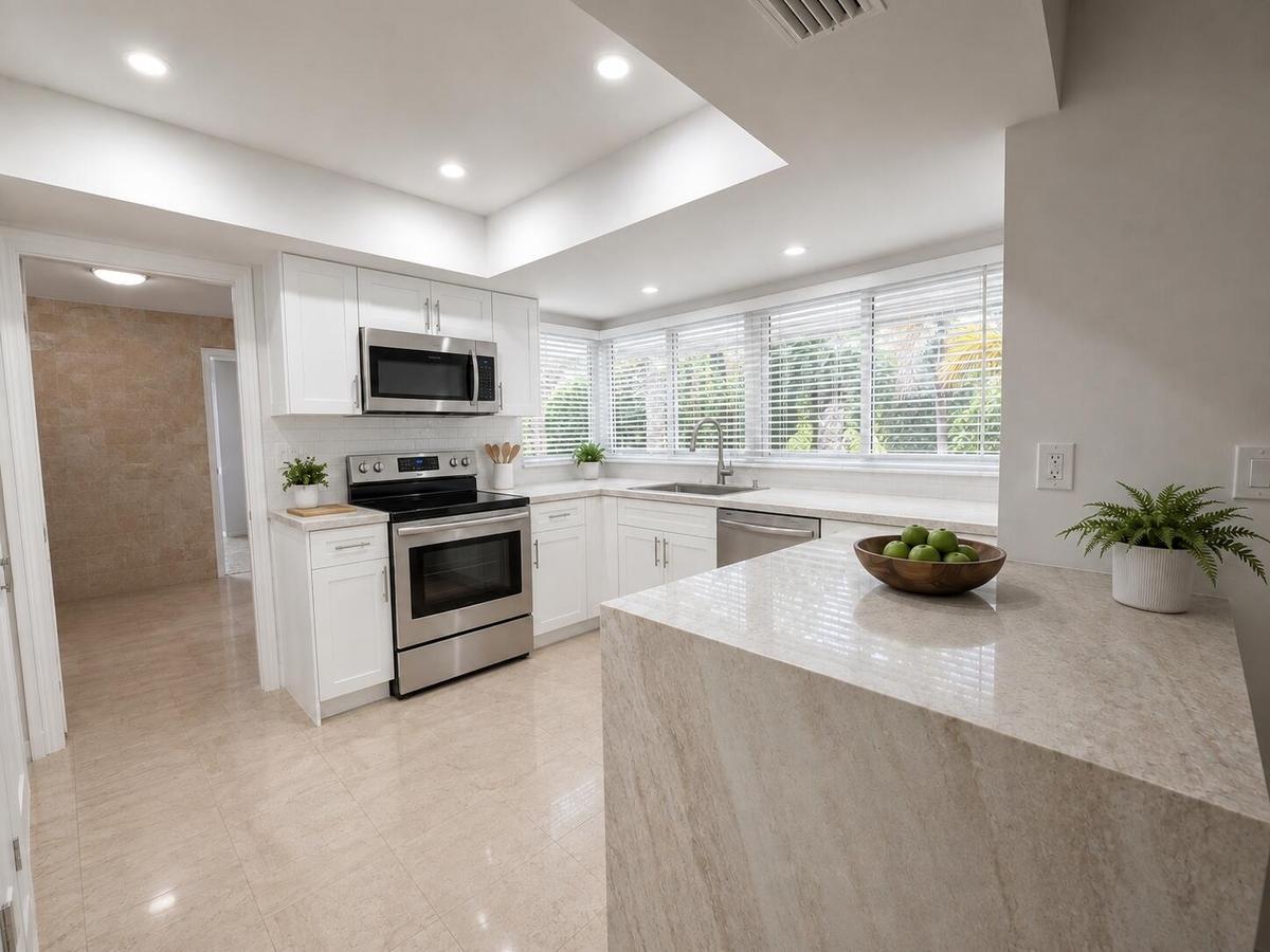 Modern kitchen featuring white cabinetry, stainless steel appliances, a breakfast bar, and multiple windows with blinds
