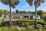 Single-story residence featuring a standing-seam metal roof, stucco exterior, attached garage, stone-paved driveway, and mature landscaping