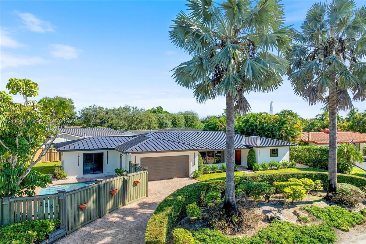 Single-story residence featuring a standing seam metal roof, attached multi-car garage, gated entry, integrated swimming pool, and mature palm landsca