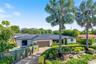 Single-story residence featuring a standing seam metal roof, attached multi-car garage, gated entry, integrated swimming pool, and mature palm landsca