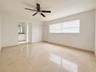 Spacious room featuring light-toned tile flooring, a ceiling fan with integrated lighting, and horizontal blinds on a large window