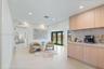 Light wood-finish cabinetry, neutral stone-finish countertops, recessed lighting, tile flooring, and black-frame glass exterior doors